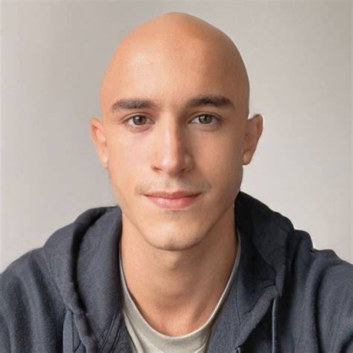 a bald man with a goatee smiles and points at the camera